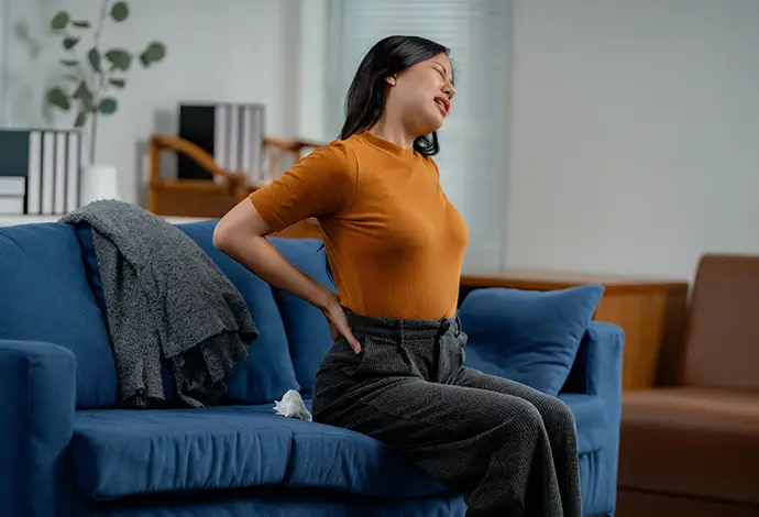woman experiencing back pain while sitting on a sofa in her living room