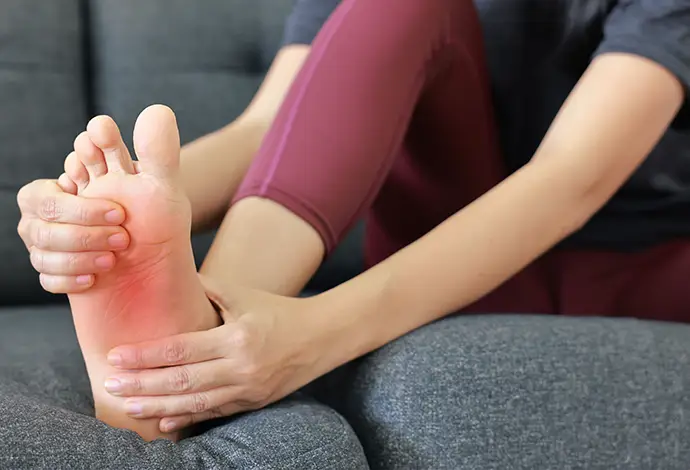 Woman massaging her painful foot and toes with red highlight on sole