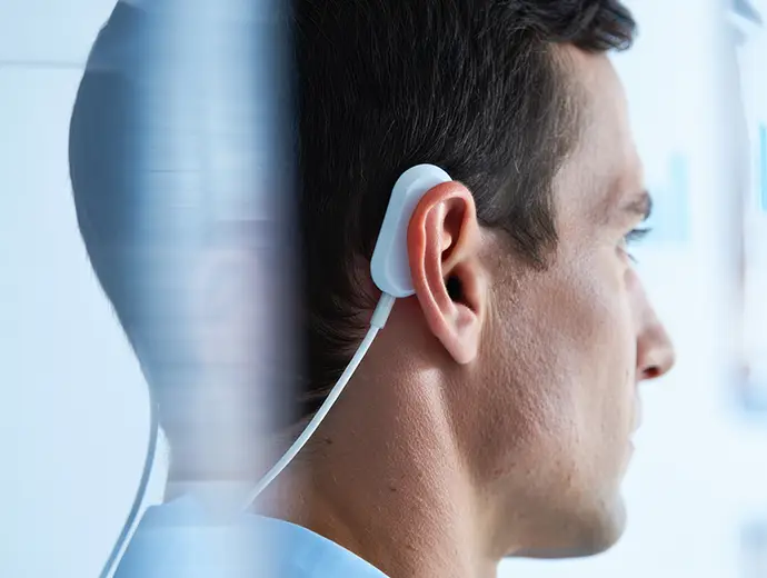 Neuromodulation device positioned behind a patient’s ear to deliver gentle electrical stimulation for pain management.