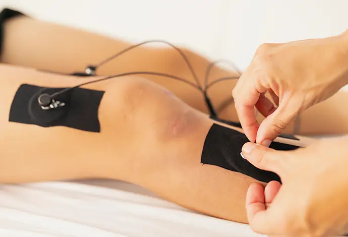 physiotherapist places the electrodes on the leg of a young patient during an electrostimulation treatment, due to a sportive injury on the knee