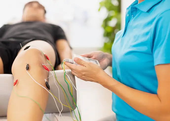 Healthcare provider operating a neuromodulation device connected to electrodes on a patient’s knee for targeted pain treatment.
